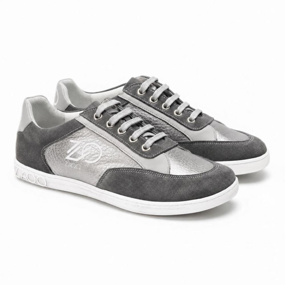 Et par OQTAV Grey-sneakers fra ZAQQ, lavet af blødt ruskind og strukturerede indsatser. Med sølvfarvede snørebånd og det karakteristiske Zagoo-logo på siden og hælen præsenteres disse stilfulde sko side om side på en hvid baggrund.