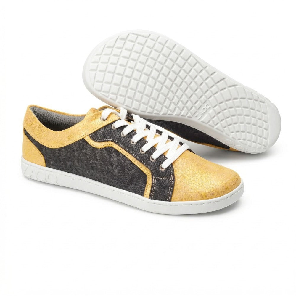 Ein Paar Sneaker in leuchtendem Gelb und Schwarz aus der QODY Gold-Kollektion der Marke ZAQQ. Der linke Schuh ist mit der Sohle nach oben ausgestellt und bietet höchsten Tragekomfort, während der rechte aufrecht steht und seine weißen Schnürsenkel und den eleganten schwarzen Abschnitt hervorhebt. Auf der Sohle mit Kreuzmuster ist das Wort ZAOO zu sehen, was auf den Einfluss des QODY Gold-Designs hinweist.