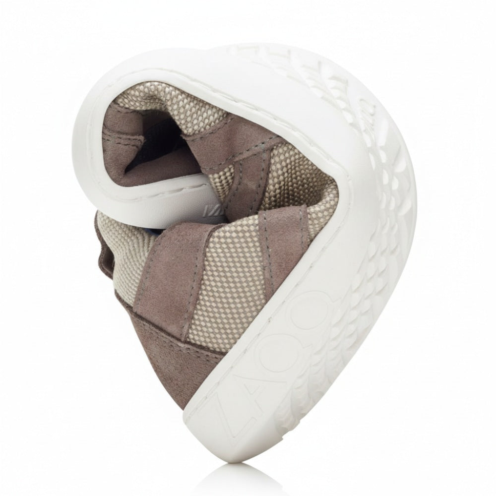 Der QUSQO Taupe von ZAQQ ist ein hochflexibler Barfußschuh, der sich in eine kompakte Form biegen lässt und seine braun-beige Farbgebung mit Strukturmuster hervorhebt. Gefertigt aus atmungsaktivem Mesh-Gewebe bietet er unvergleichliche Bewegungsfreiheit. Auf der Sohle ist der Markenname ZAQQ in großen Lettern prominent zu sehen.